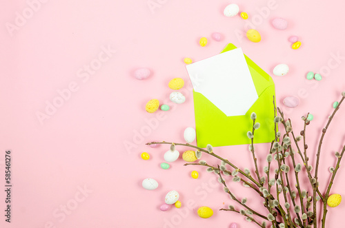 Colorful candy chocolate eggs, brunch willow andlight green envelope with blank card on pastel pink background. photo