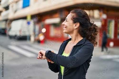 Middle age hispanic woman working out with smart watch outdoors