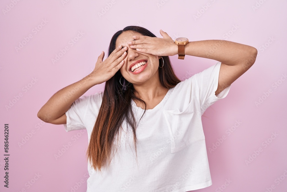 Young arab woman standing over pink background covering eyes with hands smiling cheerful and funny. blind concept. Young arab woman standing over pink background covering eyes with hands smiling cheerful and funny. blind concept.