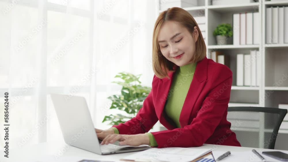 Businesswoman in red suit working on laptop and paperwork that show cost planning accounting numbers tables on office space. Businesswoman in red suit working on laptop and paperwork that show cost planning accounting numbers tables on office space.