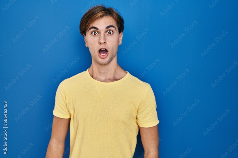 Young man standing over blue background afraid and shocked with surprise expression, fear and excited face. Young man standing over blue background afraid and shocked with surprise expression, fear and excited face.