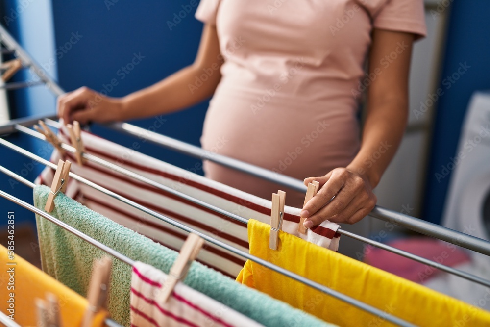 Young latin woman pregnant hanging clothes on clothesline at laundry room