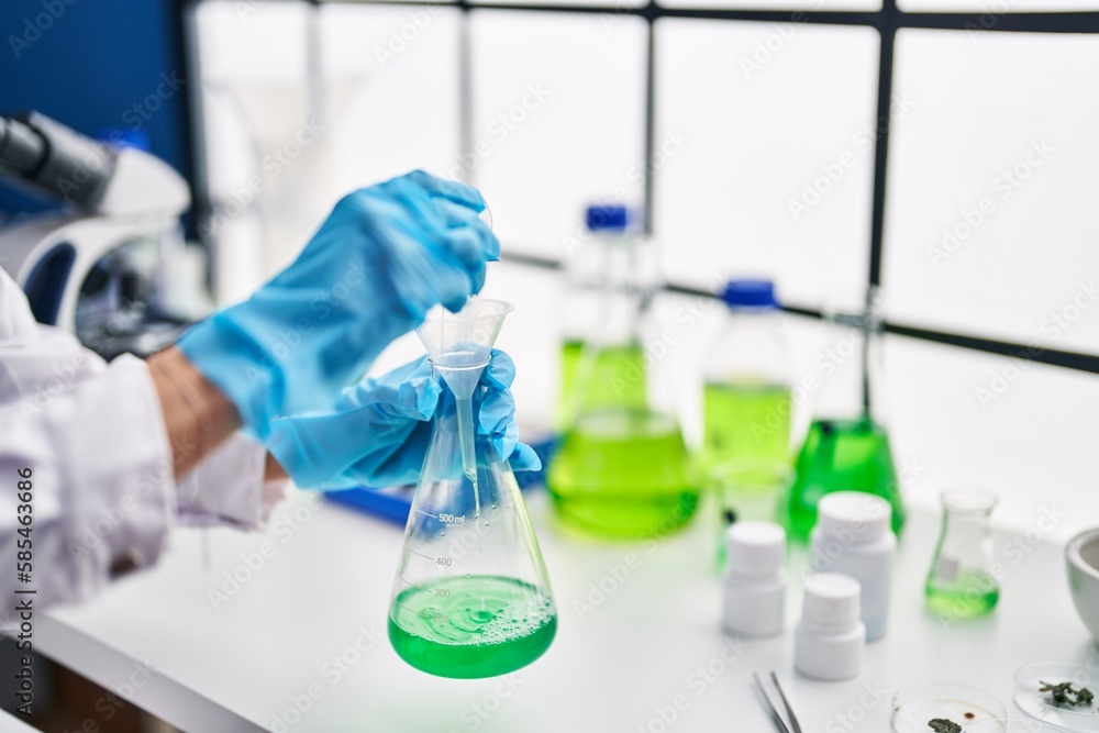 Fototapeta premium Young beautiful hispanic woman scientist pouring liquid on test tube at laboratory
