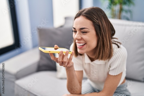 Young beautiful hispanic woman talking on the smartphone sitting on sofa at home