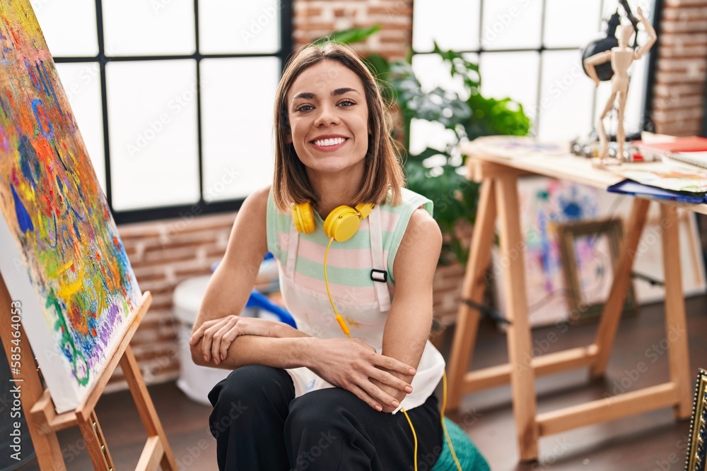 Young beautiful hispanic woman artist smiling confident sitting with arms crossed gesture at art studio