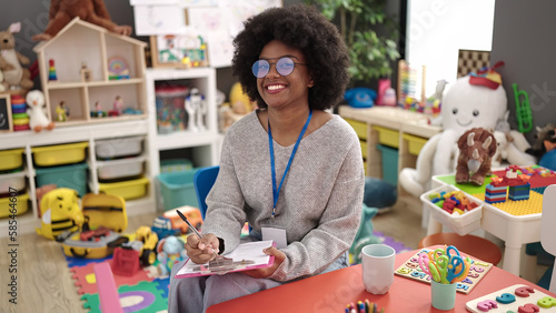 Canvas Print African american woman preschool teacher smiling confident writing on document a