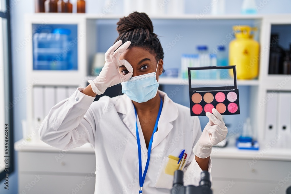 Young african american with braids working at scientist laboratory doing make up smiling happy doing ok sign with hand on eye looking through fingers Young african american with braids working at scientist laboratory doing make up smiling happy doing ok sign with hand on eye looking through fingers