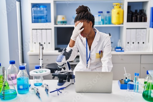 African american woman scientist stressed using laptop working at laboratory