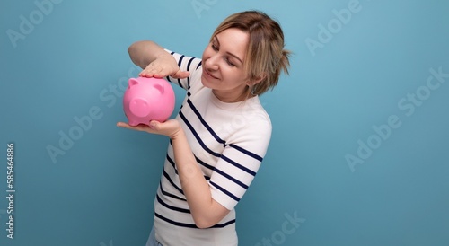 horizontal photo of attractive young woman in casual outfit cute hugging a piggy bank of coins on a blue background with copy space