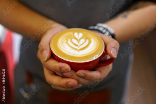 close up of a person holding a cup of coffee. Rosetta latte art coffee