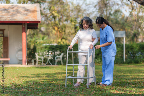 Asian nurse or a female physiotherapist is helping an elderly woman patient use a walker to learn to walk.