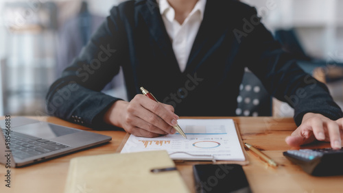 Businesswoman using calculator to check company income and budget from graph and chart.