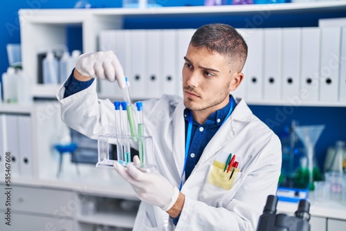 Young hispanic man scientist holding test tubes at laboratory