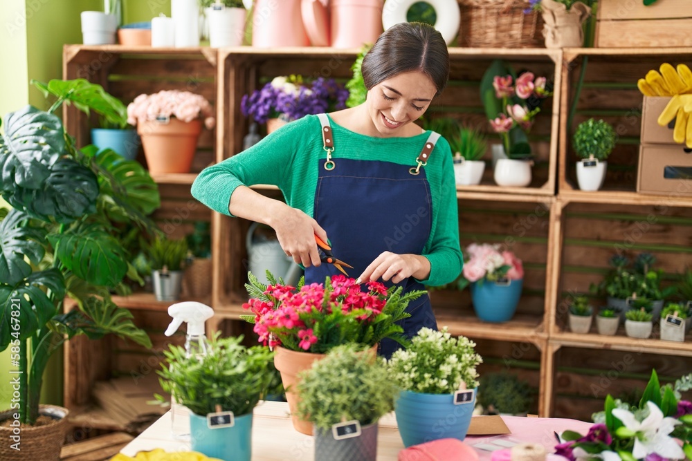 Young beautiful hispanic woman florist cutting plants at flower shop