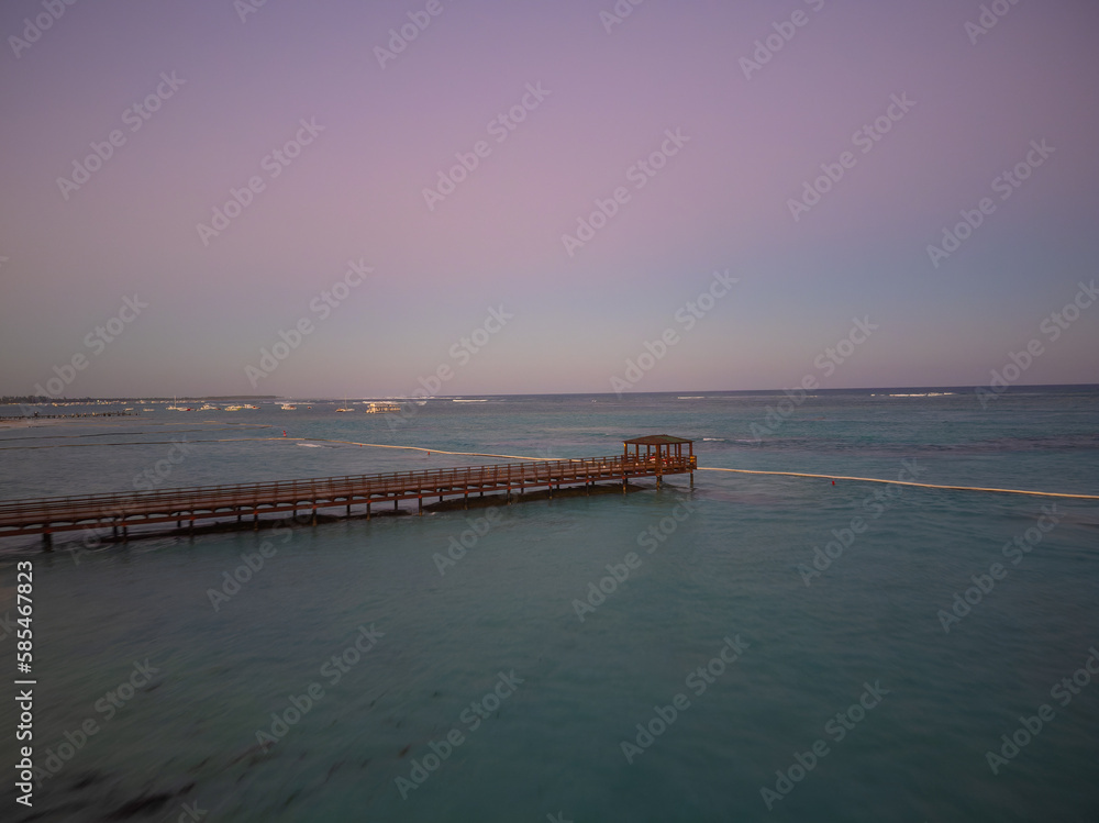 Sea, beach and wooden pier at dusk. The beautiful sky is colored purple and pink by the rays of the setting sun. Desert place. The beauty of nature, ecology, recreation.