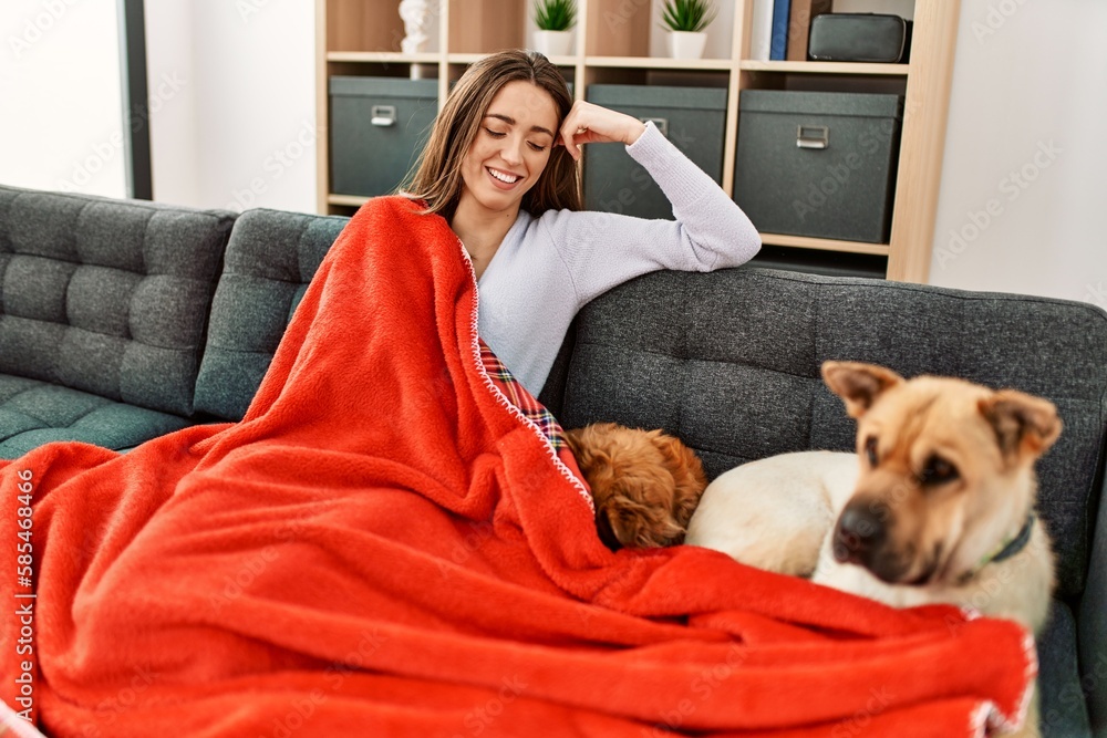 Young hispanic woman covering with blanket sitting on sofa with dogs at home Young hispanic woman covering with blanket sitting on sofa with dogs at home