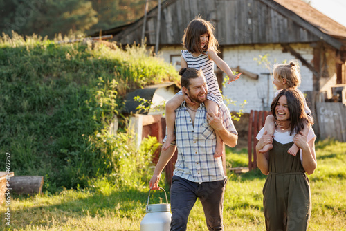 Happy young family enjoy spending time together on weekend at the countryside. Mother, father and two kids walking near their wooden country house. Moving from urban areas to rural areas concept.