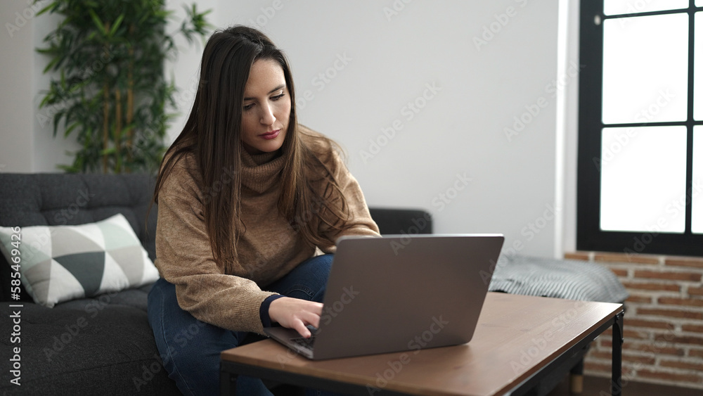 Beautiful hispanic woman using laptop sitting on sofa with worried expression at home Beautiful hispanic woman using laptop sitting on sofa with worried expression at home