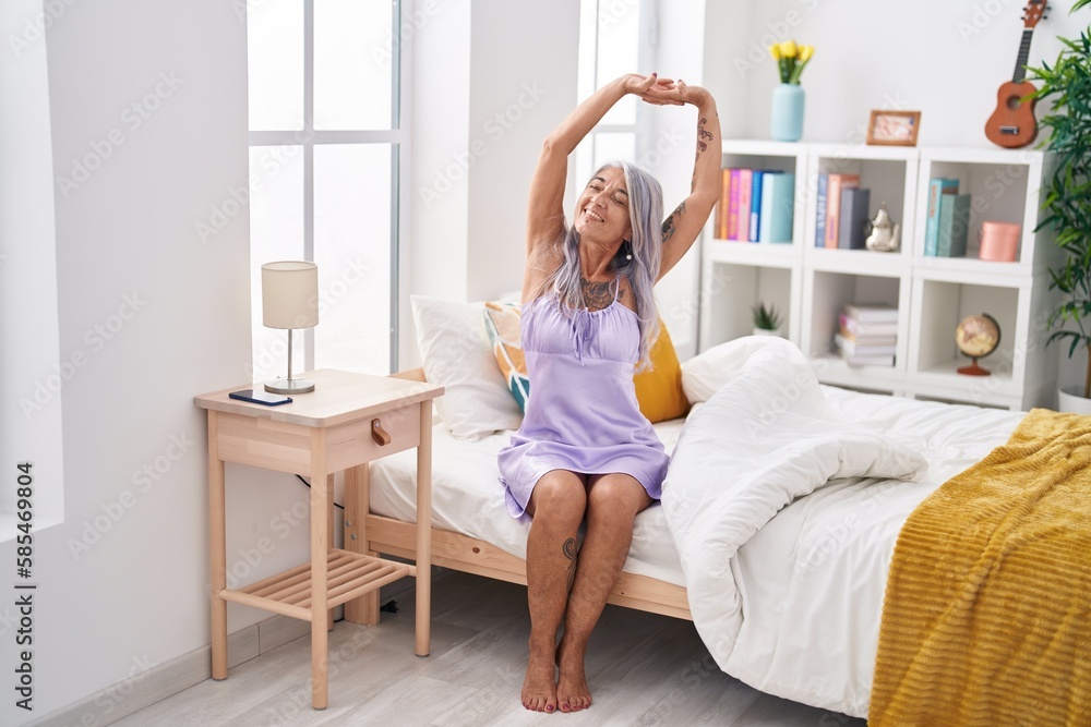 Middle age grey-haired woman waking up stretching arms at bedroom Middle age grey-haired woman waking up stretching arms at bedroom