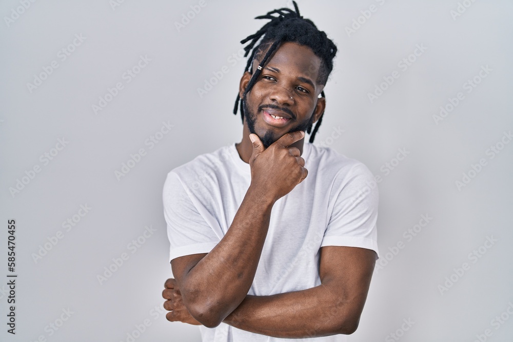 African man with dreadlocks wearing casual t shirt over white background looking confident at the camera smiling with crossed arms and hand raised on chin. thinking positive. African man with dreadlocks wearing casual t shirt over white background looking confident at the camera smiling with crossed arms and hand raised on chin. thinking positive.