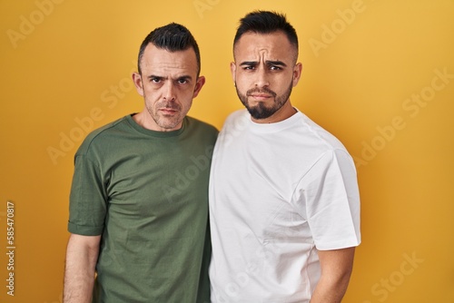 Homosexual couple standing over yellow background skeptic and nervous, frowning upset because of problem. negative person.