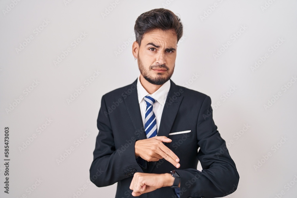 Young hispanic man with tattoos wearing business suit and tie in hurry pointing to watch time, impatience, upset and angry for deadline delay Young hispanic man with tattoos wearing business suit and tie in hurry pointing to watch time, impatience, upset and angry for deadline delay