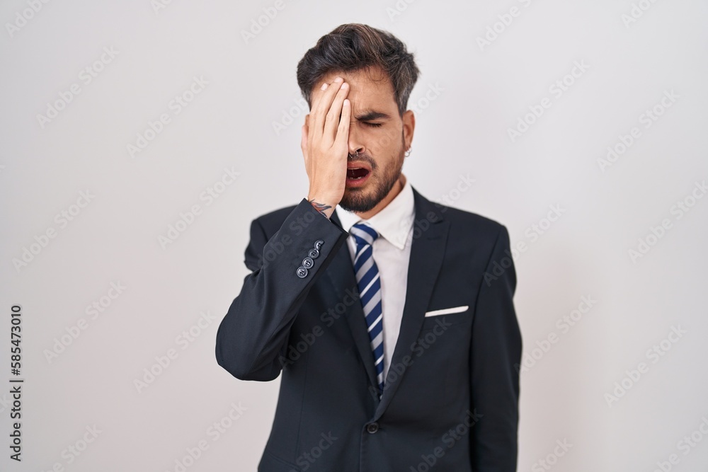 Young hispanic man with tattoos wearing business suit and tie yawning tired covering half face, eye and mouth with hand. face hurts in pain. Young hispanic man with tattoos wearing business suit and tie yawning tired covering half face, eye and mouth with hand. face hurts in pain.