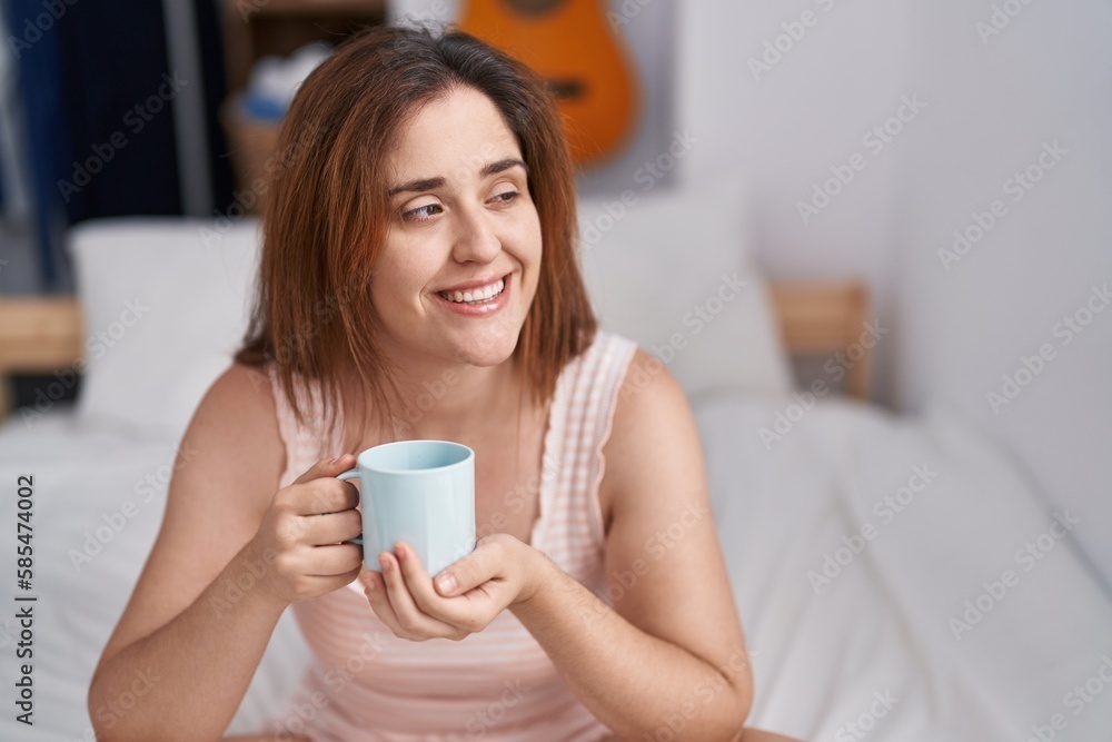 Young woman drinking cup of coffee sitting on bed at bedroom Young woman drinking cup of coffee sitting on bed at bedroom