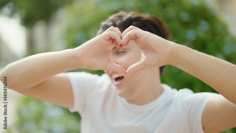 Non binary man smiling confident doing heart gesture with hands at park