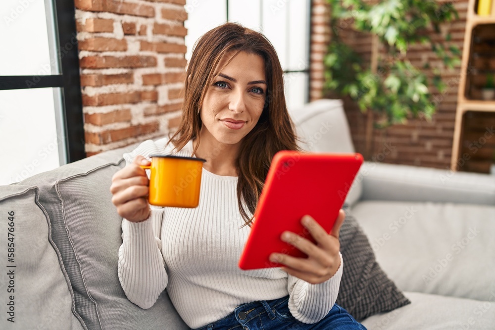 Young hispanic woman drinking coffee and using touchpad at home Young hispanic woman drinking coffee and using touchpad at home