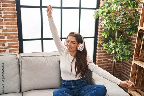 Young hispanic woman listening to music sitting on sofa at home