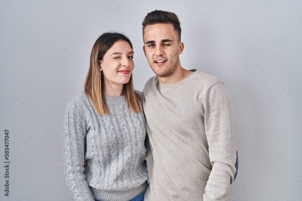 Young hispanic couple standing over white background winking looking at the camera with sexy expression, cheerful and happy face. Young hispanic couple standing over white background winking looking at the camera with sexy expression, cheerful and happy face.