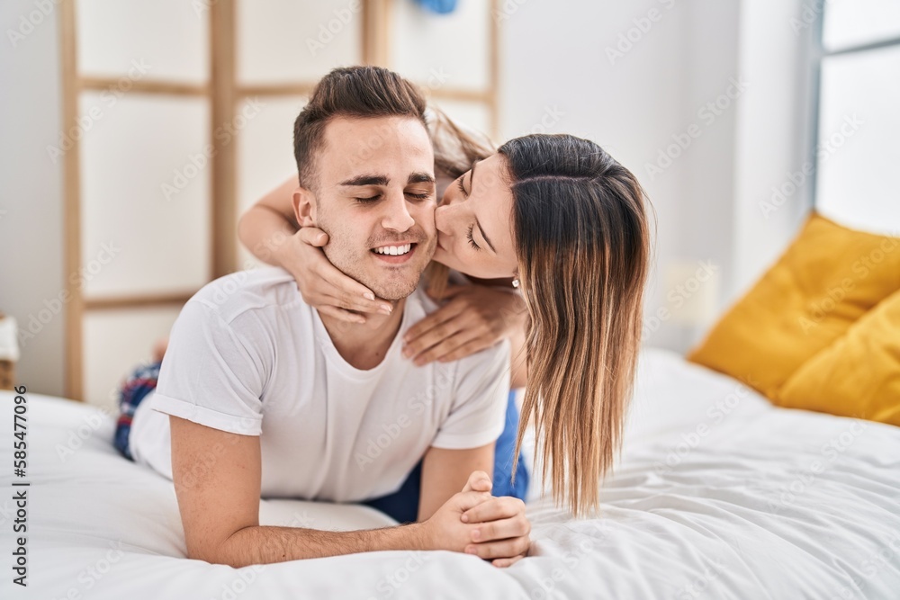 Man and woman couple lying on bed hugging each other and kissing at bedroom