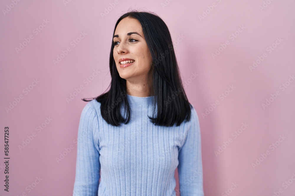 Hispanic woman standing over pink background looking away to side with smile on face, natural expression. laughing confident. Hispanic woman standing over pink background looking away to side with smile on face, natural expression. laughing confident.