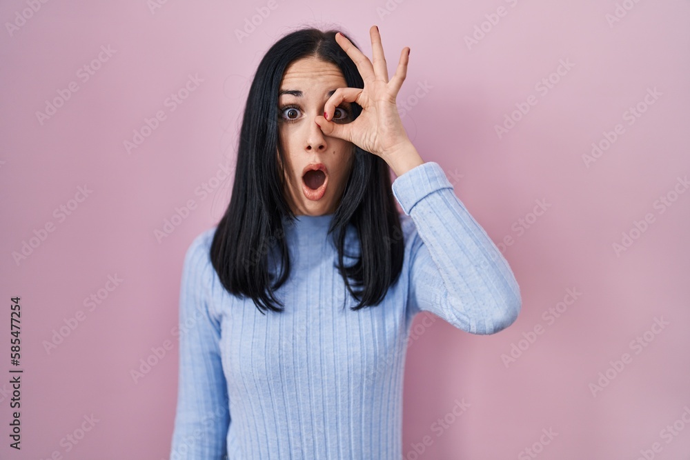 Hispanic woman standing over pink background doing ok gesture shocked with surprised face, eye looking through fingers. unbelieving expression. Hispanic woman standing over pink background doing ok gesture shocked with surprised face, eye looking through fingers. unbelieving expression.
