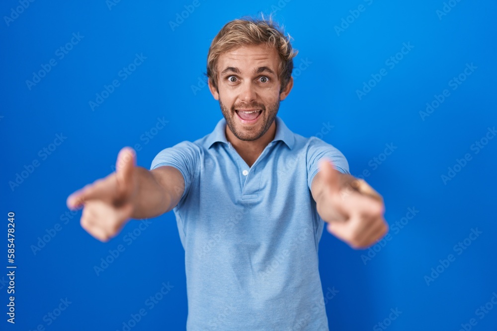 Caucasian man standing over blue background pointing to you and the camera with fingers, smiling positive and cheerful Caucasian man standing over blue background pointing to you and the camera with fingers, smiling positive and cheerful