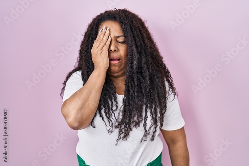 Plus size hispanic woman standing over pink background yawning tired covering half face, eye and mouth with hand. face hurts in pain.