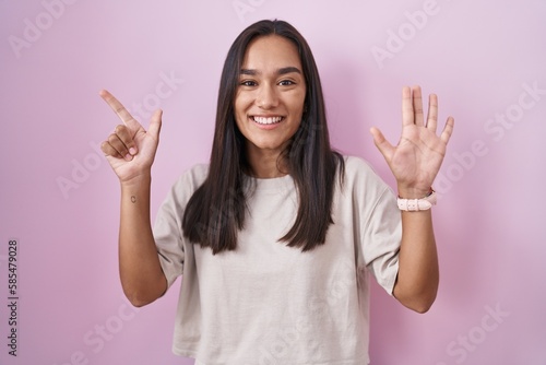 Young hispanic woman standing over pink background showing and pointing up with fingers number seven while smiling confident and happy. © Krakenimages.com