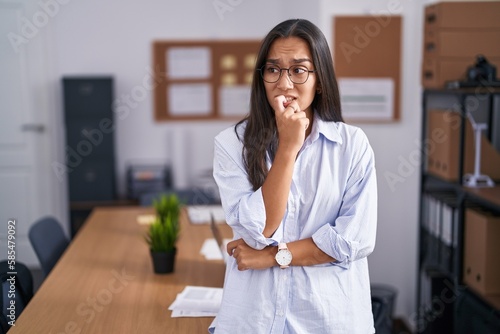 Foto Young hispanic woman at the office looking stressed and nervous with hands on mouth biting nails