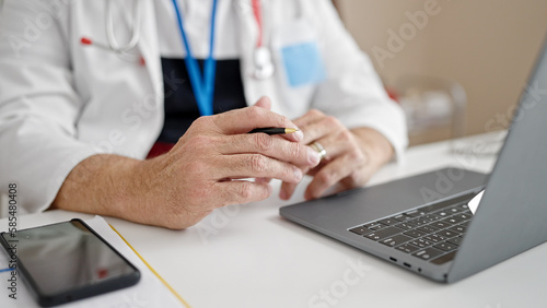 Middle age man with grey hair doctor using laptop working at clinic