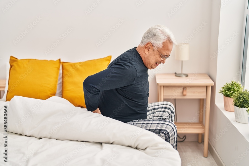 Senior man suffering for backache sitting on bed at bedroom