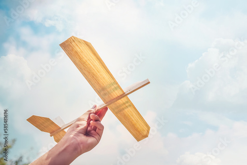 Boy flying a toy Balsa wood airplane into the sun and sky