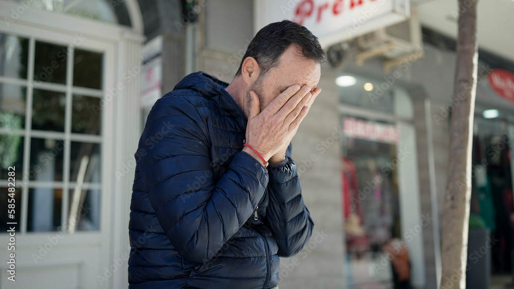 Middle age man sitting on bench with worried expression at street Middle age man sitting on bench with worried expression at street