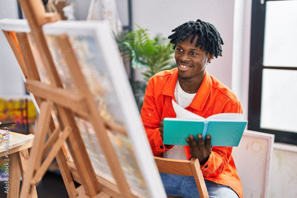 African american man artist smiling confident reading book drawing at art studio