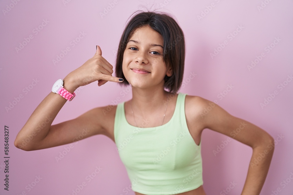 Young girl standing over pink background smiling doing phone gesture with hand and fingers like talking on the telephone. communicating concepts. Young girl standing over pink background smiling doing phone gesture with hand and fingers like talking on the telephone. communicating concepts.