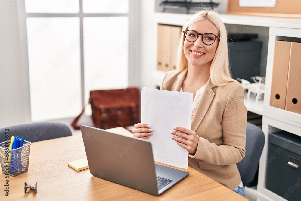 Young blonde woman business worker using laptop working and reading document at office Young blonde woman business worker using laptop working and reading document at office