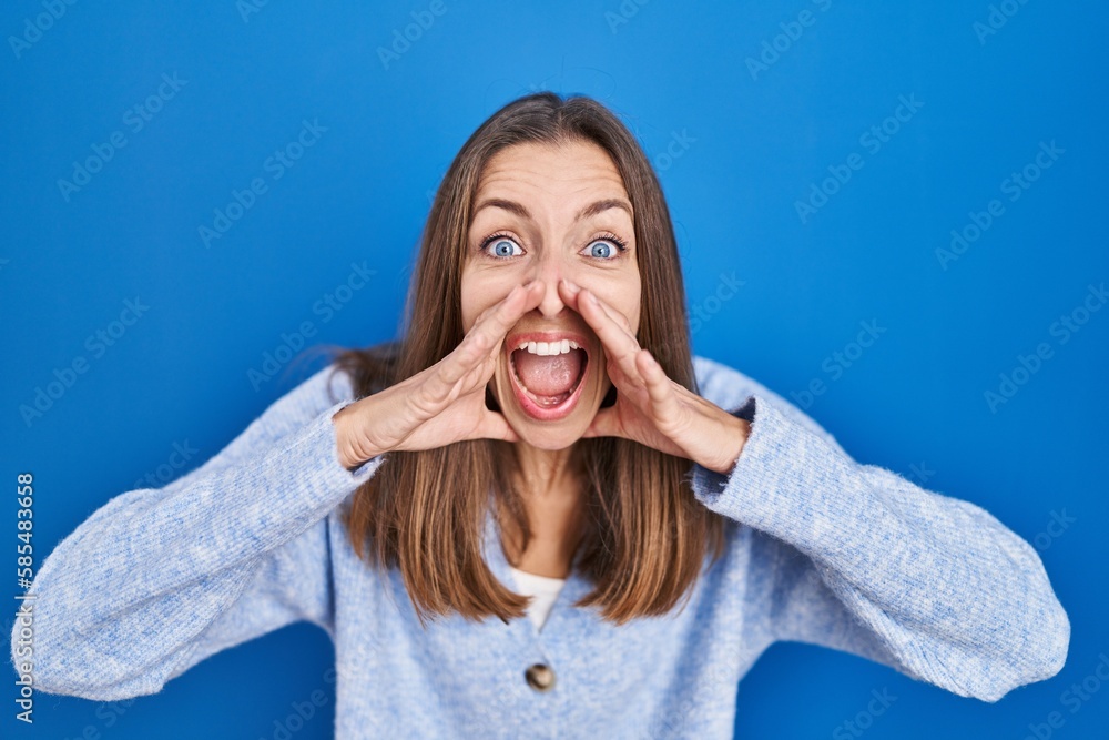 Young woman standing over blue background shouting angry out loud with hands over mouth Young woman standing over blue background shouting angry out loud with hands over mouth