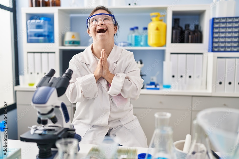 Hispanic girl with down syndrome working at scientist laboratory begging and praying with hands together with hope expression on face very emotional and worried. begging. Hispanic girl with down syndrome working at scientist laboratory begging and praying with hands together with hope expression on face very emotional and worried. begging.