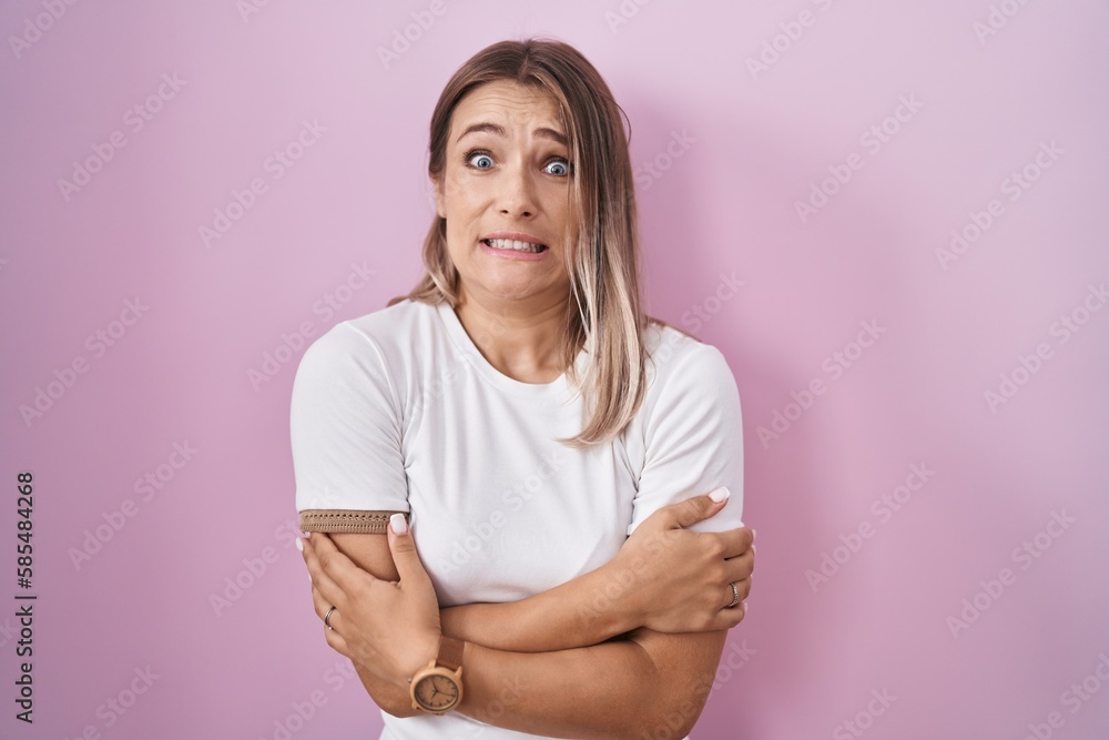 Fototapeta premium Blonde caucasian woman standing over pink background shaking and freezing for winter cold with sad and shock expression on face