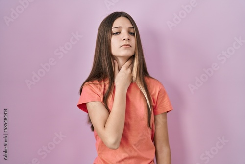 Teenager girl standing over pink background touching painful neck, sore throat for flu, clod and infection